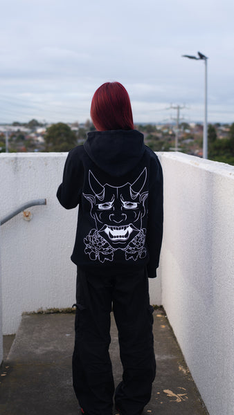 Bold and fearless, a woman confidently wears the Trillax Black Oni Hoodie, expressing her unique style and making a bold fashion statement with our Trillax oni watching her back.